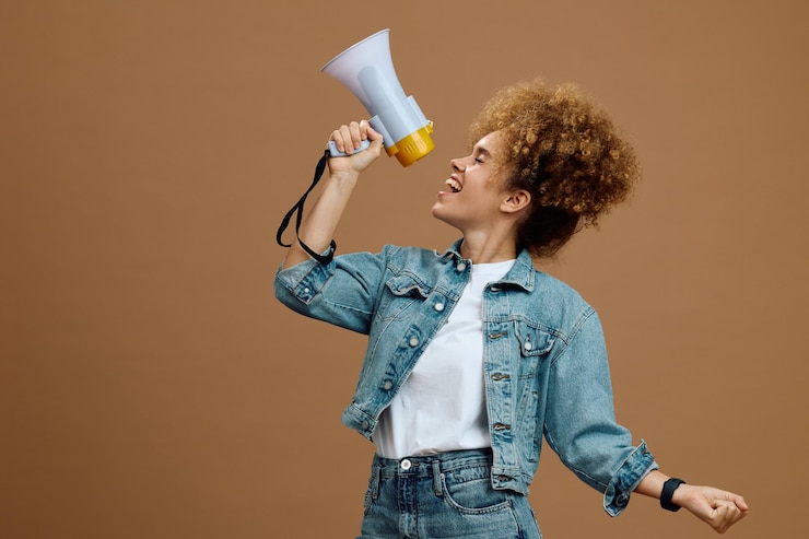 Foto jonge vrouw schreeuwt door een megafoon tegen een neutrale achtergrond