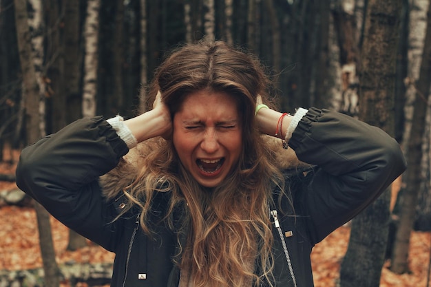 Jonge vrouw schreeuwt terwijl ze haar oren bedekt in het bos.