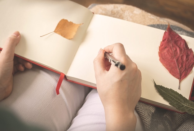 Jonge vrouw schrijft in haar oude dagboek met herfstbladeren. Gezellige herfst achtergrondfoto