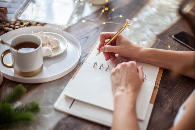 Jonge vrouw schrijft plannen of doelen voor het nieuwe jaar terwijl haar dochter kerstbomen maakt