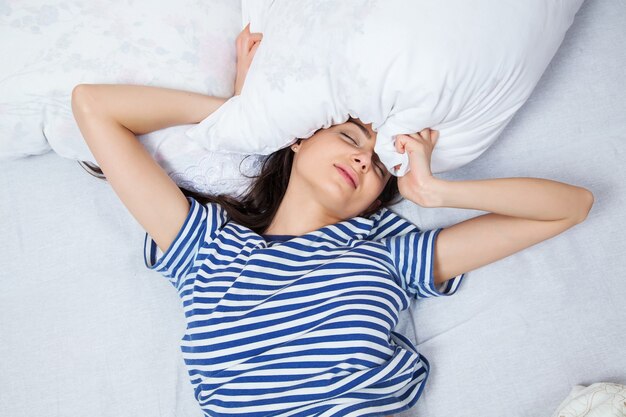 Jonge vrouw slapen in nachtkleding op het witte linnen in bed thuis, bovenaanzicht.