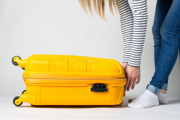 Jonge vrouw sluit een koffer op een lichte achtergrond. Vakantie en reizen concept