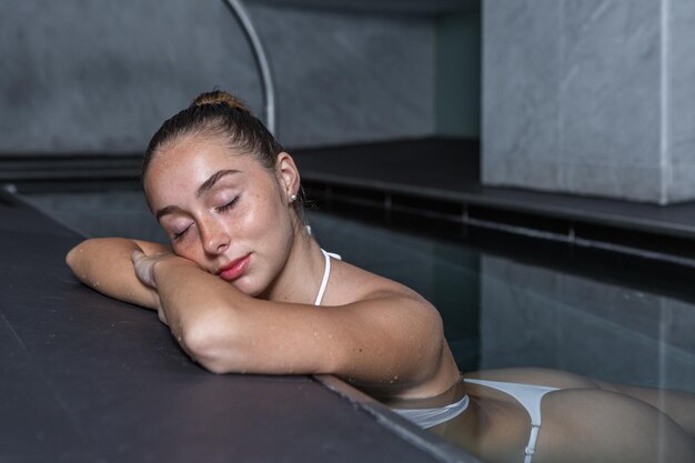 Jonge vrouw sluit haar ogen en ontspant zich in het zwembad.