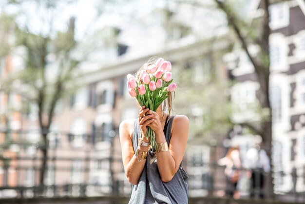 Jonge vrouw sluitend gezicht met bouguet van roze tulpen in de buurt van het waterkanaal in de stad Amsterdam