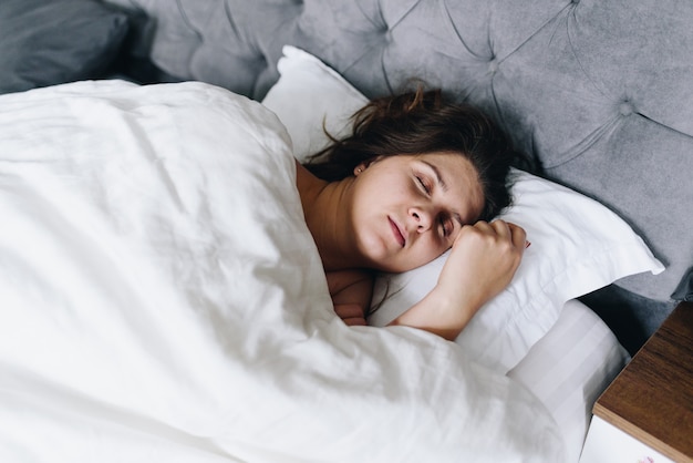 Foto jonge vrouw snel in slaap slapen in haar bed op wit beddengoed