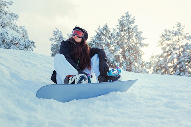 Jonge vrouw snowboarder die in de sneeuw van de berg zit