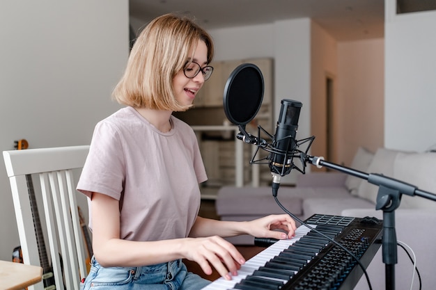 Jonge vrouw speelt synthesizer en zingt in de microfoon bij homestudio