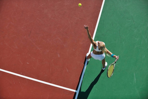 Jonge vrouw speelt tennis buiten.