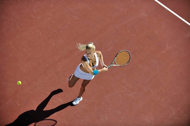 Jonge vrouw speelt tennis buiten.
