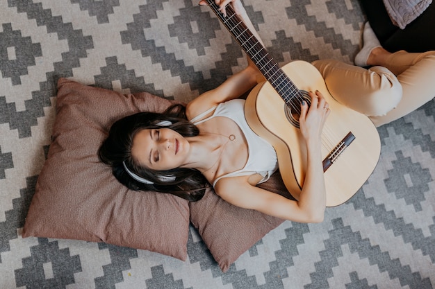 Jonge vrouw speelt witte gitaar. Vrouw luisteren naar muziek in witte koptelefoon op de vloer.