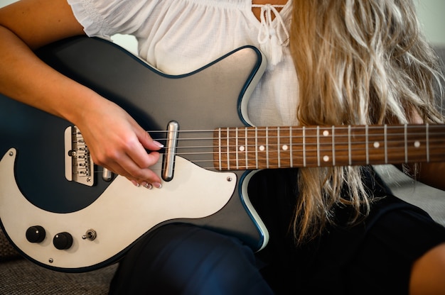 Jonge vrouw spelen een gitaar zittend op haar bank thuis