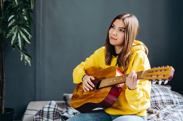 Jonge vrouw spelen op akoestische gitaar thuis, zittend op het bed