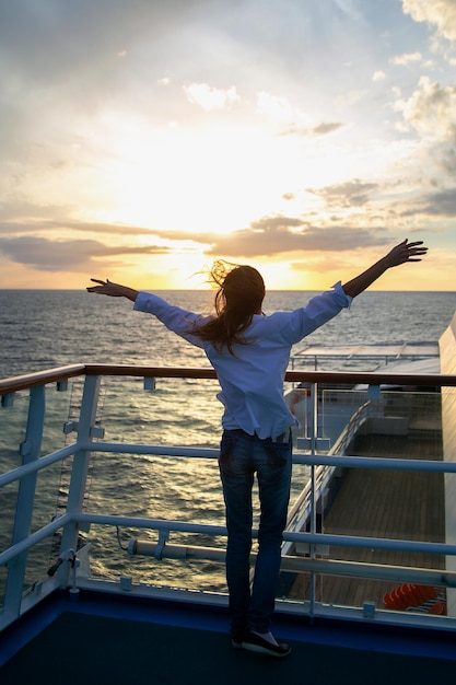 Foto jonge vrouw staat aan boord van een schip met haar armen uitgestrekt naar de wind en de zonsondergang