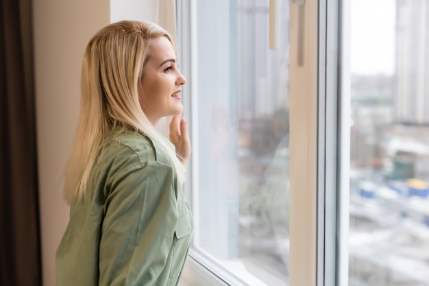 Jonge vrouw staat en kijkt uit het raam