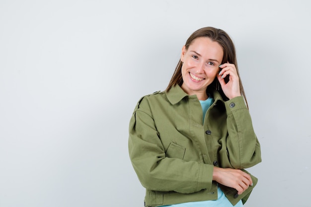 Jonge vrouw staat in denkende pose in groene jas en ziet er vrolijk uit. vooraanzicht.