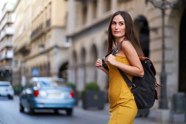 Jonge vrouw steekt een straat met verkeer over met haar rugzak op haar rug