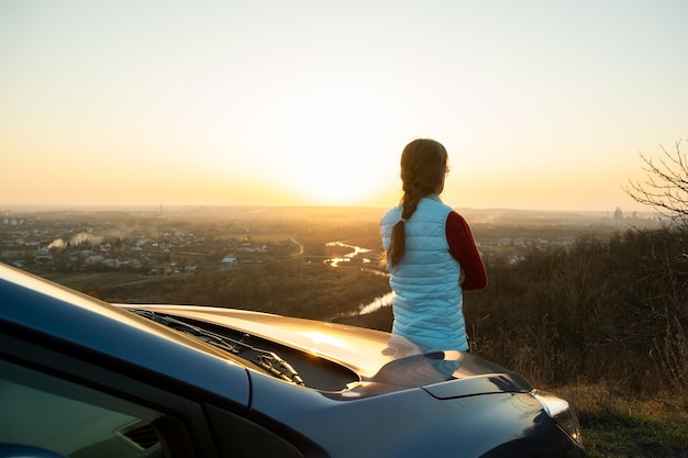 Foto jonge vrouw stond in de buurt van haar auto genieten van warme zonsondergang