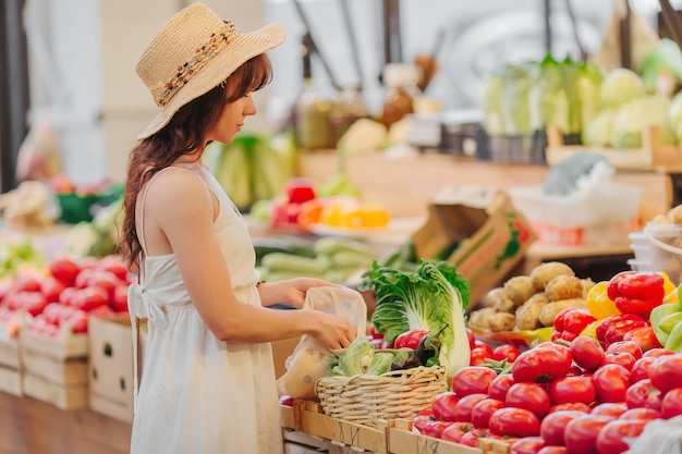 Jonge vrouw stopt groenten en fruit in een katoenen zak op de voedselmarkt. Herbruikbare eco-tas om te winkelen. Geen afvalconcept.