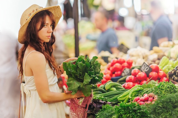 Jonge vrouw stopt groenten en fruit in een katoenen zak op de voedselmarkt. Herbruikbare eco-tas om te winkelen. Geen afvalconcept.