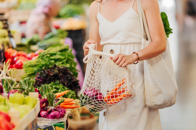 Jonge vrouw stopt groenten en fruit in een katoenen zak op de voedselmarkt. Herbruikbare eco-tas om te winkelen. Geen afvalconcept.