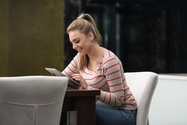 Jonge vrouw student drinken en plezier maken met tablet in cafetaria