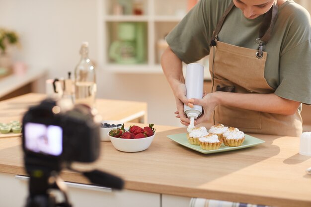 Jonge vrouw taarten versieren met room aan de keukentafel en fotograferen op de camera