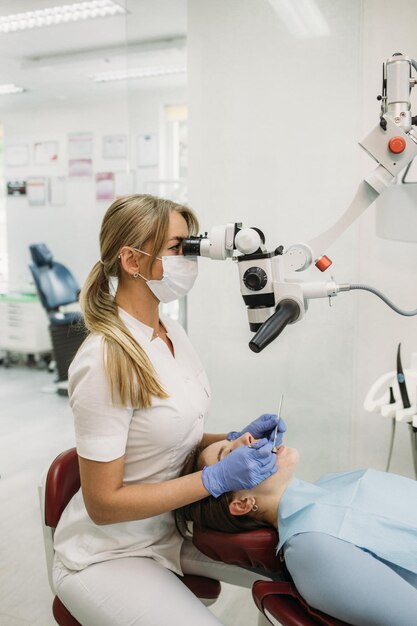 Jonge vrouw tandarts behandelen wortelkanalen met behulp van microscoop in de tandheelkundige kliniek man patiënt liggend op tandarts stoel met open mond geneeskunde tandheelkunde en gezondheidszorg concept tandheelkundige apparatuur