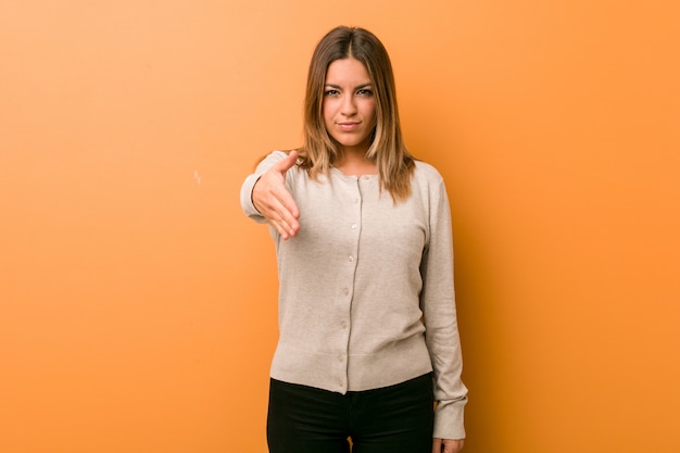 Jonge vrouw tegen muur het uitrekken zich hand bij camera in groetgebaar.