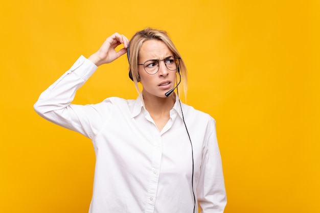 Jonge vrouw telemarketeer die zich verbaasd en verward voelt, hoofd krabt en naar de zijkant kijkt