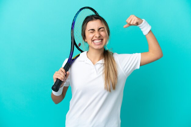 Jonge vrouw tennisser geïsoleerd op blauwe achtergrond doen sterk gebaar