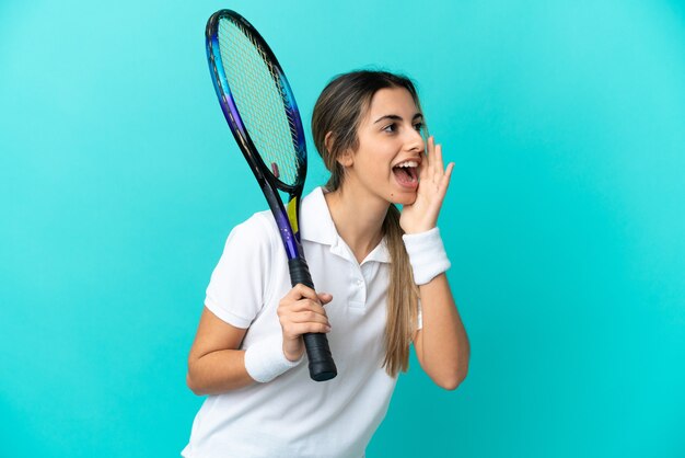 Jonge vrouw tennisser geïsoleerd op blauwe achtergrond schreeuwen met mond wijd open naar de zijkant