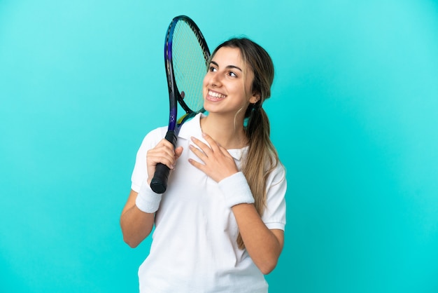 Jonge vrouw tennisser geïsoleerd op blauwe achtergrond terwijl ze glimlacht