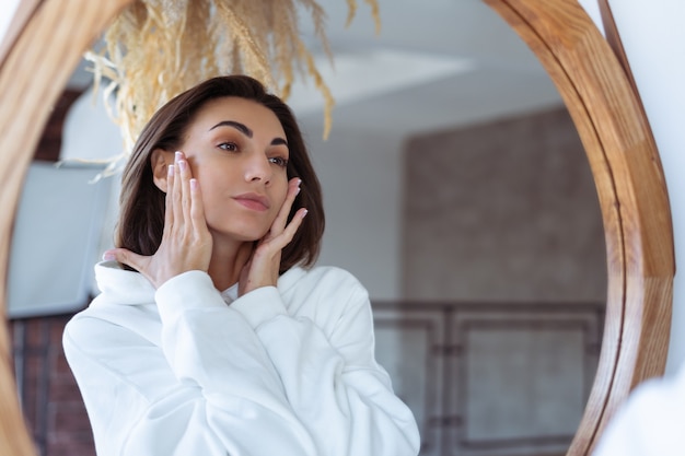 Jonge vrouw thuis in de slaapkamer in een warme witte hoodie poseren voor de spiegel