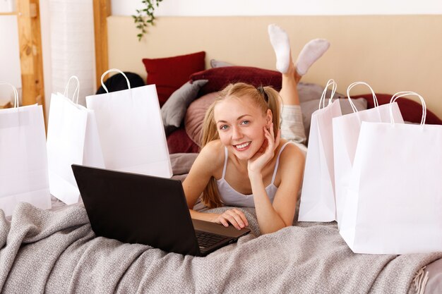 Jonge vrouw thuis met laptop en witte papieren zakken