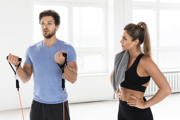 Jonge vrouw tijdens training met een persoonlijke fitnessinstructeur met behulp van rubberen weerstandsbanden in de sportschool.