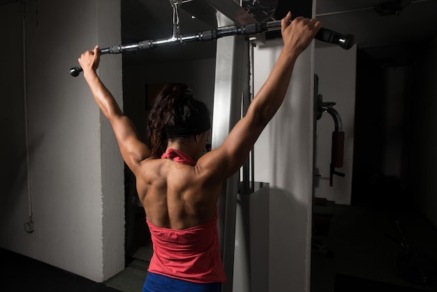 Jonge vrouw trainen terug op machine in de sportschool en buigen spieren gespierde atletische bodybuilder Fitness Model