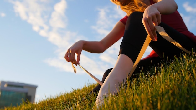 Jonge vrouw trekt haar pointe-schoenen aan en bindt ze vast terwijl ze op het groene gras zit bij zonsondergang