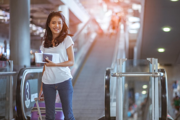 Jonge vrouw trekt koffer in moderne luchthaventerminal Reizende man met zijn bagage tijdens het wachten op vervoer Achteraanzicht Kopieer ruimte