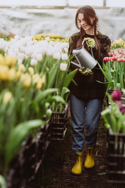 Jonge vrouw tuinman in een handschoenen water een bloembed van tulpen met behulp van een gieter.