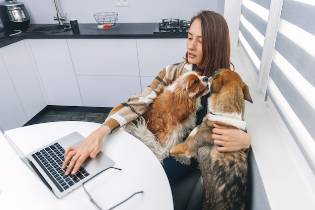 Jonge vrouw typt op laptop en knuffelt haar honden