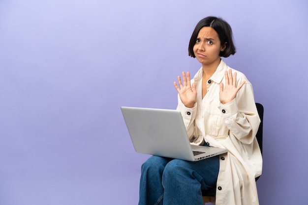 Jonge vrouw van gemengd ras die op een stoel zit met een laptop, isoleerde nerveuze handen naar voren uitrekkend