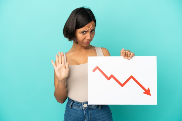 Jonge vrouw van gemengd ras geïsoleerd met een bord met een dalend statistiekpijlsymbool en stopbord