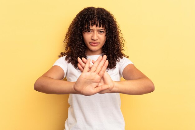 Jonge vrouw van gemengd ras geïsoleerd op een gele achtergrond die staat met uitgestrekte hand met stopbord dat je verhindert