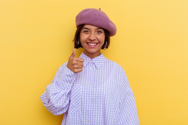 Jonge vrouw van gemengd ras met een baret geïsoleerd op een gele achtergrond glimlachend en duim omhoog and