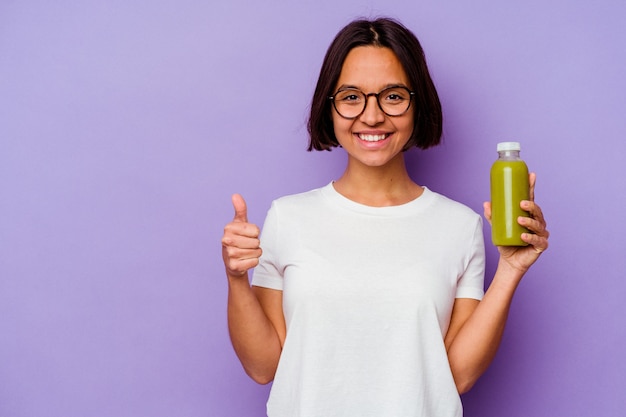 Jonge vrouw van gemengd ras met een gezonde smoothie geïsoleerd op een paarse achtergrond glimlachend en duim omhoog