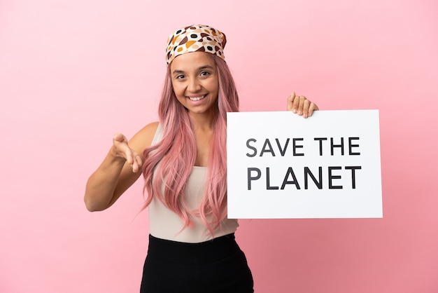 Jonge vrouw van gemengd ras met roze haar geïsoleerd op roze achtergrond met een bordje met de tekst Save the Planet die een deal maakt