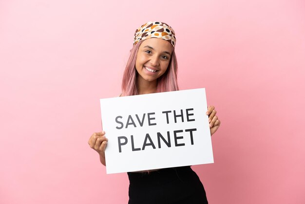 Jonge vrouw van gemengd ras met roze haar geïsoleerd op roze achtergrond met een bordje met de tekst Save the Planet met gelukkige uitdrukking