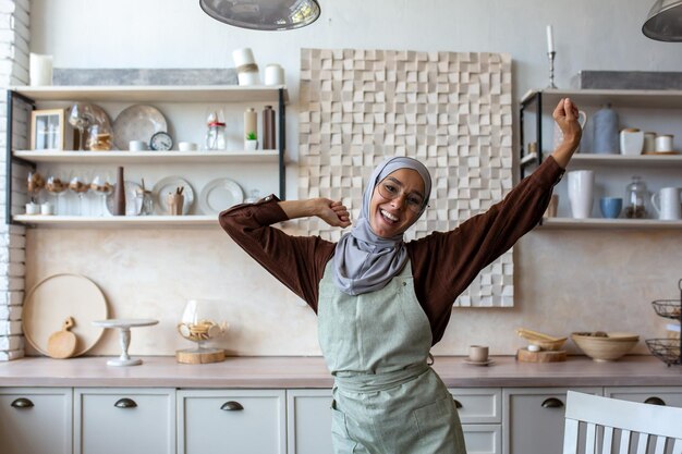 Jonge vrouw van oosterse afkomst huisvrouw in hijab in schort kookt en maakt schoon in de keuken die ze danst