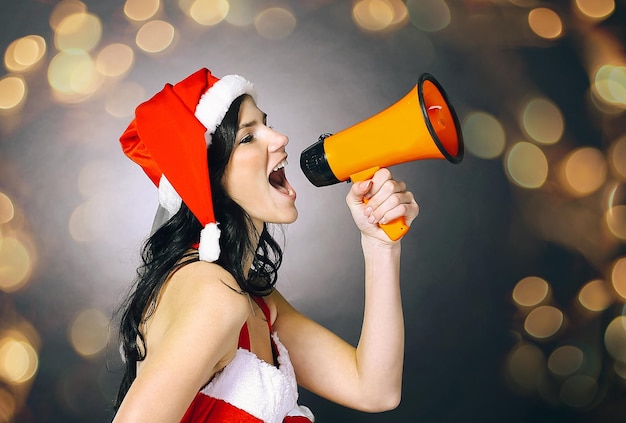 Jonge vrouw verkleed als kerstman schreeuwend in een megafoon mooi bokeh-effect van een slinger