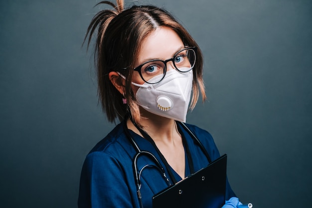 Jonge vrouw verpleegster ziekenhuis werknemer in medische beschermend masker houden blocnote geïsoleerd op een grijze achtergrond.